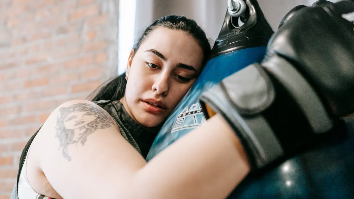 Low angle side view of exhausted young female in boxing gloves having pause in hard training in fitness center